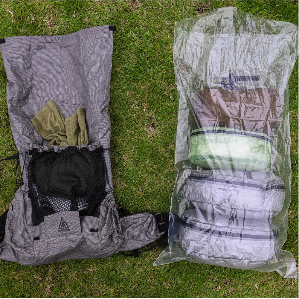 Top-down view of an open backpack next to a clear polycro liner filled with packed gear on grass