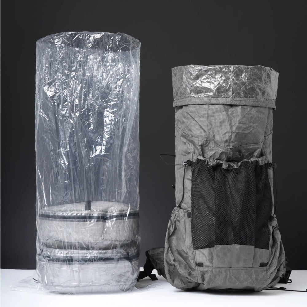 Clear ultralight polycro backpack liner standing beside a packed grey hiking backpack on dark background
