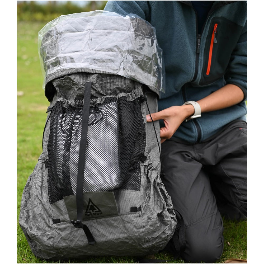 Hiker kneeling beside a grey backpack with a polycro liner rolled over the top opening in the field