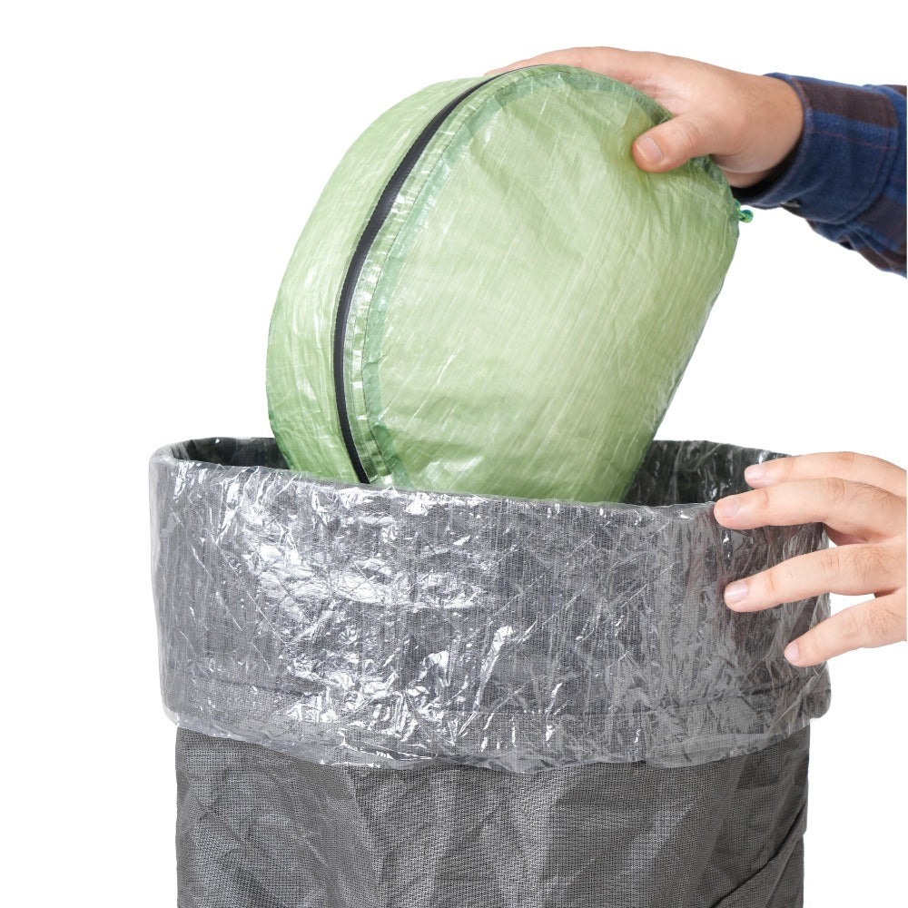 Green packing pod being loaded into a backpack lined with a transparent polycro liner