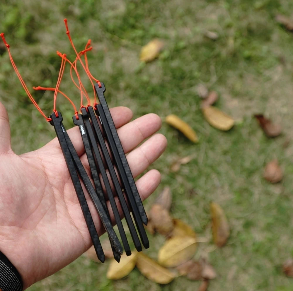 HODRGEAR ultralight carbon fiber tent stakes with orange cord, held in hand on grass