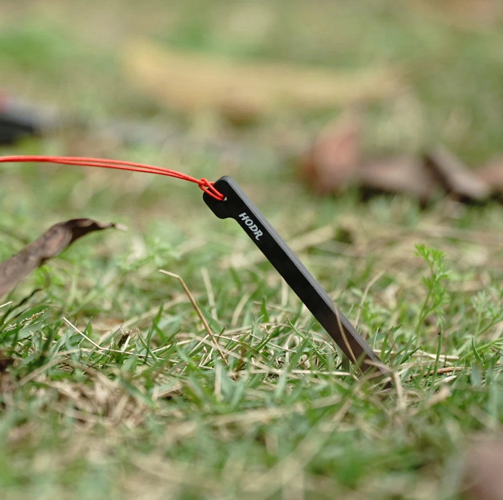 HODRGEAR ultra-light carbon fiber tent stake with red cord, 3.7g, in grass